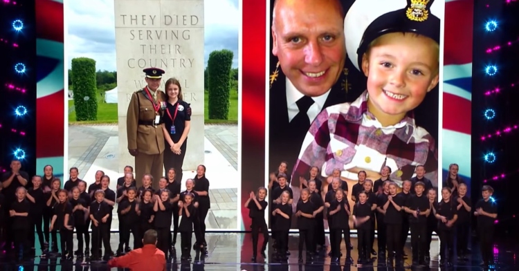 the voices of armed forces children choir singing on the “britain’s got talent” stage as part of their audition. behind them is a screen showing two different photos of children with a parents that’s in the armed forces.