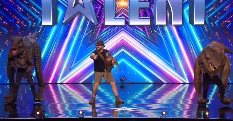 chris roberts dancing with two dinosaurs while holding a smaller dinosaur on “britain’s got talent.”