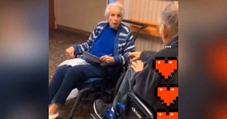 elderly woman sitting in a wheelchair. in front of her, to the side, is her husband, dan, who is also sitting in a wheelchair. her mouth is open from shock at the fact that he’s here with her.