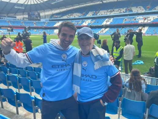charlie gibson and his grandad smiling as they pose at a manchester city football game.