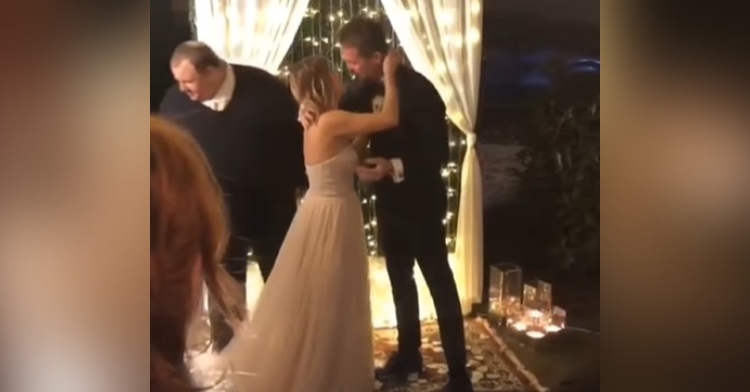 janelle and mike bass leaning in to kiss at their wedding as the officiant steps away. it’s night time and they are standing in front of a curtain of lights.