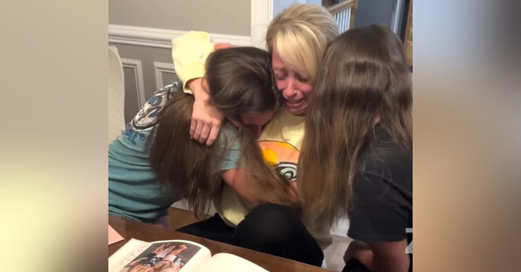 becky ruvolo crying as she hugs her stepdaughters, julianna and gabriella. all three of them are sitting at a dining room table.