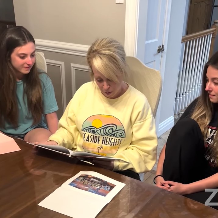 becky ruvolo reading a note in a scrapbook as she sits at a dining room table. twins juliana and gabriella ruvolo sit beside her on each side.