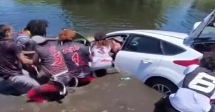 flag football team helping a man out of his white sedan after driving into a pond.