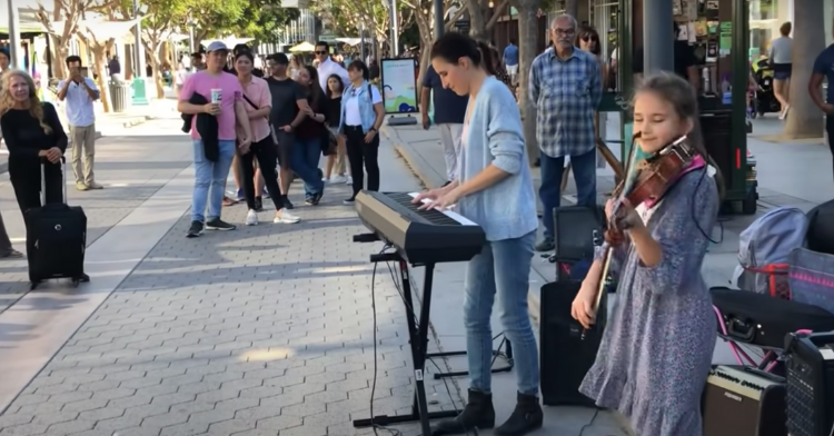 karolina protsenko playing the violin next to her mom playing the piano in the LA streets.