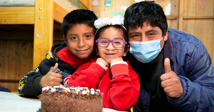 maria kristhell smiling with her brother and dad as she sits at a table with a chocolate cake.