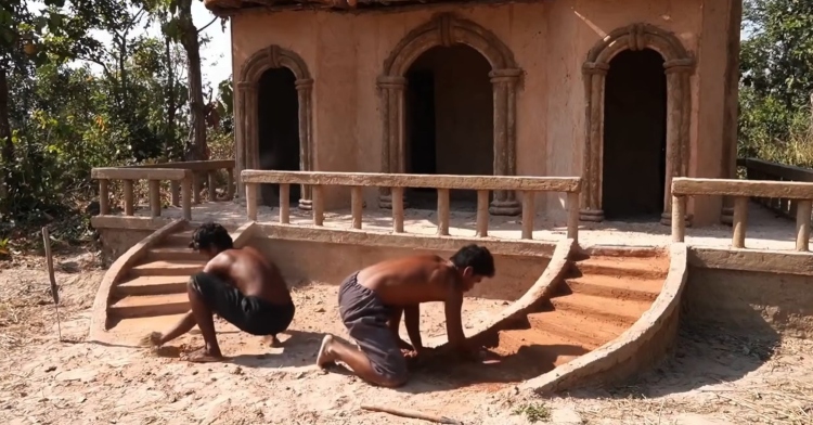 two men kneeling on the ground as they build a staircase out of mud.