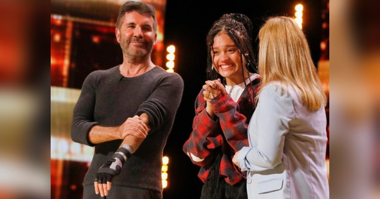 simon cowell, sara james, and her mom standing on the “america’s got talent” stage together. there’s a back-view of sara’s mom and we see simon and sara smiling.