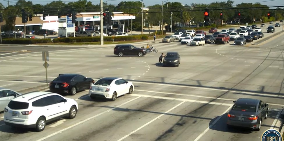 a woman running in the middle of an intersection to stop a car who's driver is unconscious. 