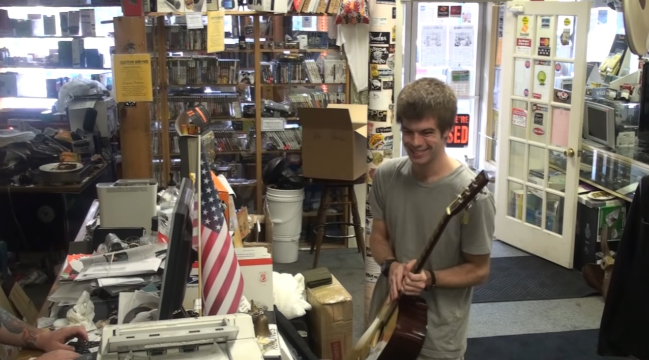 a young man smiling wide as he holds a guitar he's about to purchase at guitar grave.