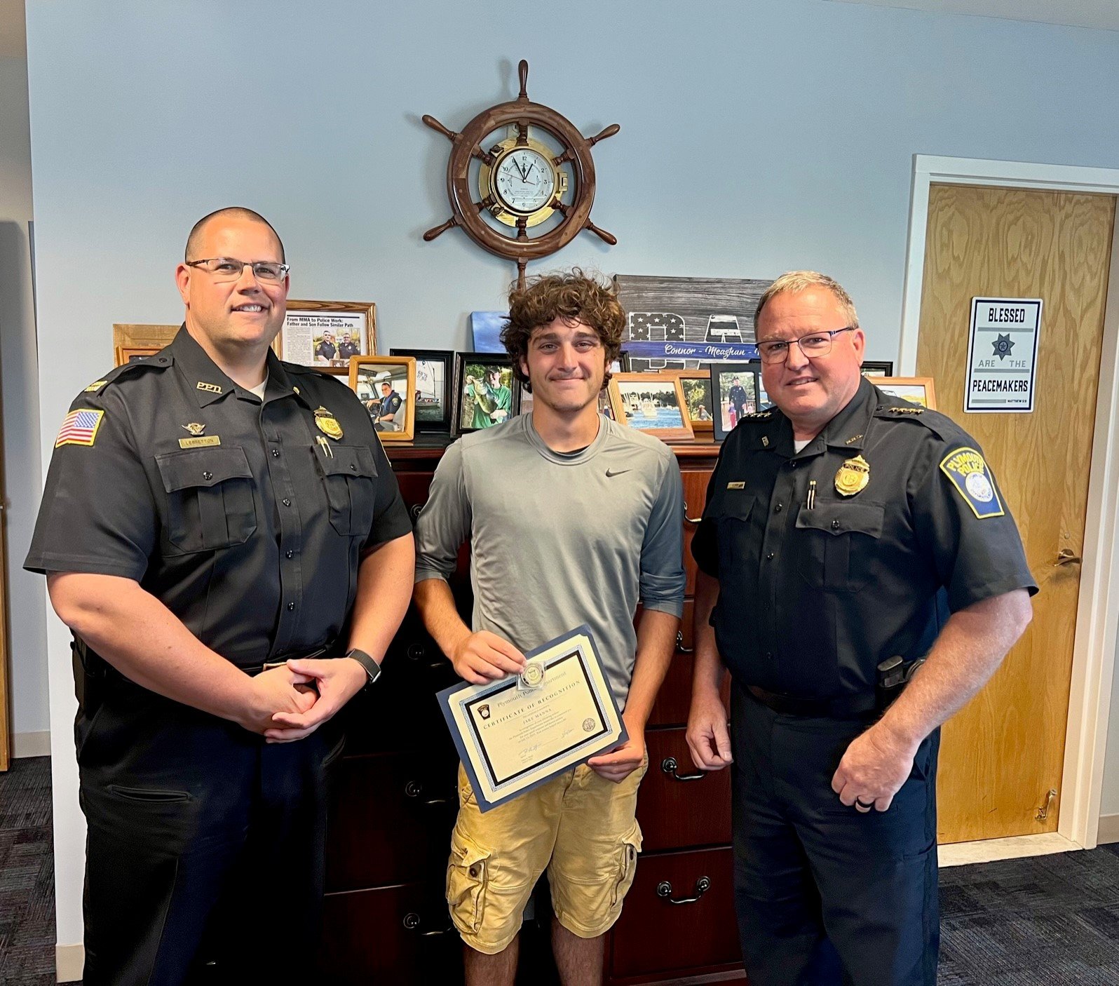 jake manna posing with two plymouth police officers as he holds his certificate for helping save a little girl's life.