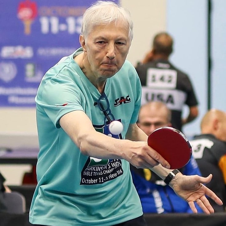 nenad bach playing ping pong. the ball is coming toward him and he's reaching his paddle toward it.