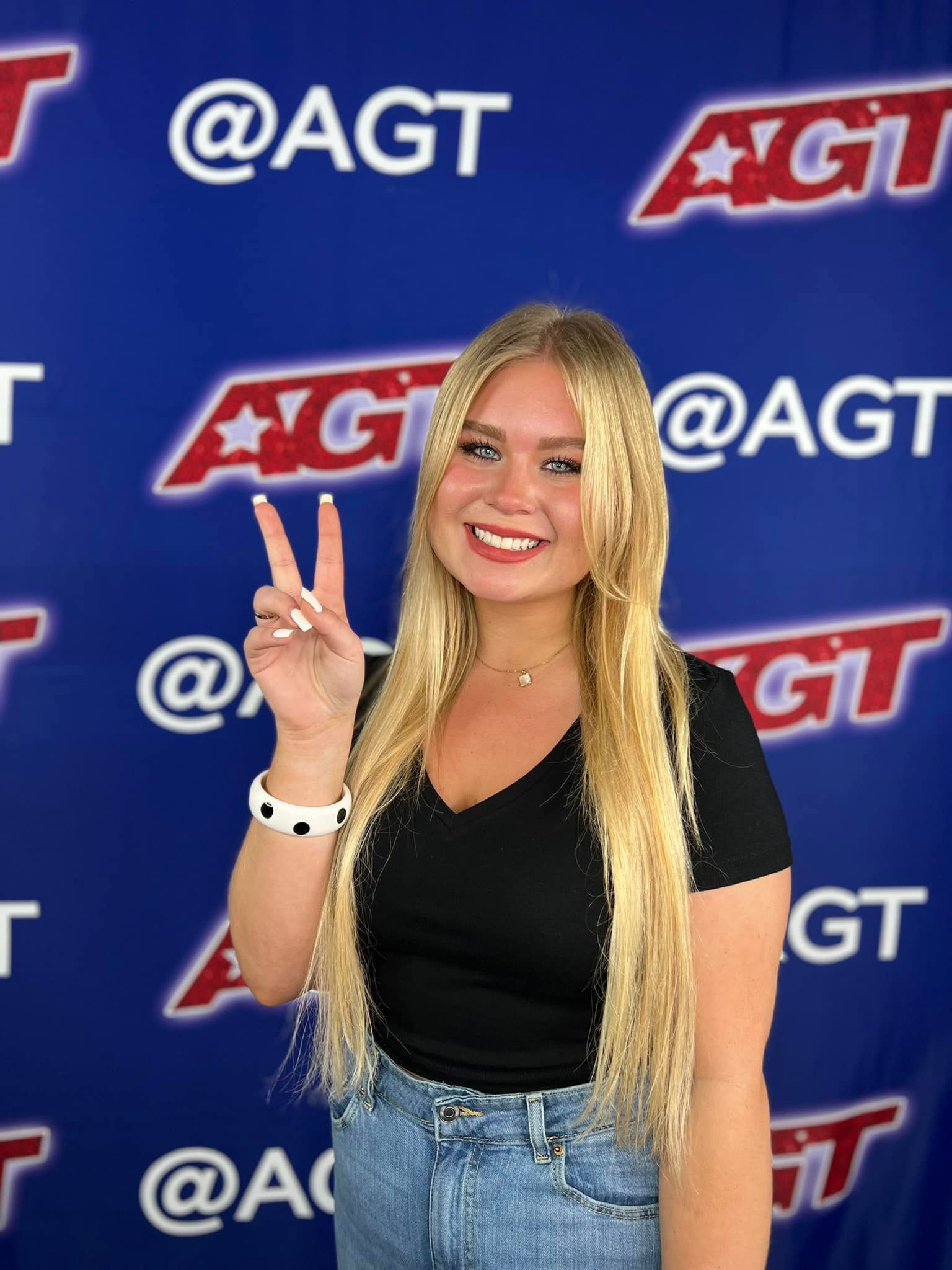 Ava Swiss with a peace hand sign smiling in front of the agt banner