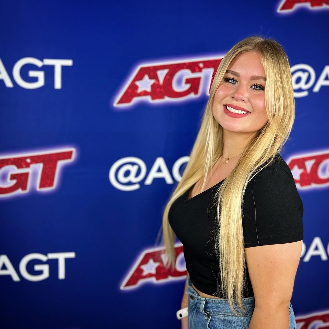 Ava Swiss smiling in front of agt's banner