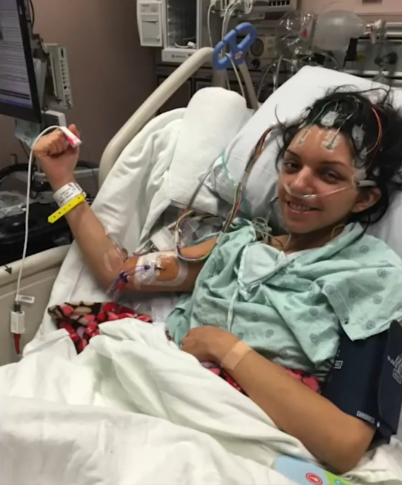 dr martinez smiling while sitting in a hospital bed. she's lightly flexing one arm to show off her muscles.