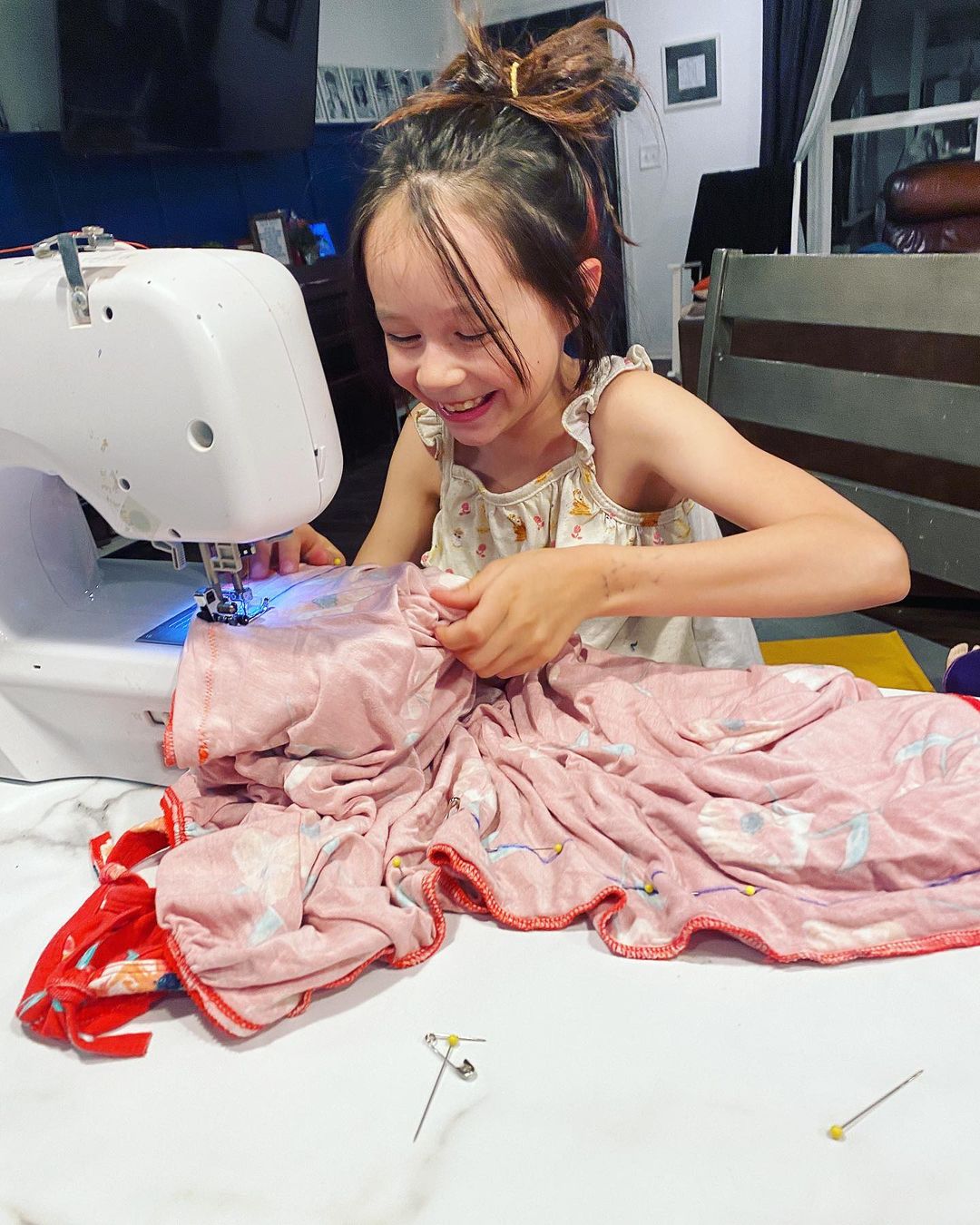 kaia aragon smiling as she uses a sewing machine.