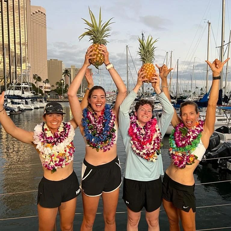 Libby Costello, Sophia Denison Johnston, Brooke Downes, and Adrienne Smith holding up pineapples and wearing leis after arriving in hawaii.