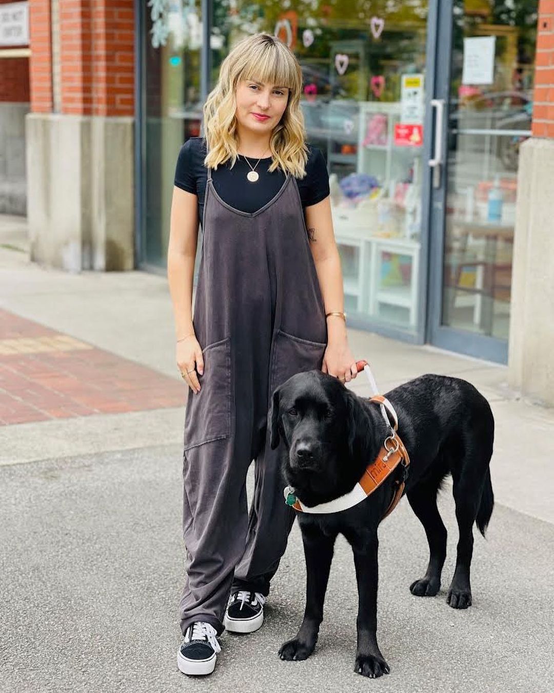 Molly Burke wears slouchy overalls and holds her guide dog Gallop on a leash.