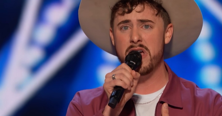 closeup of bay turner singing on agt. he holds the microphone with one hand. his mouth is open as he sings with a passionate look on his face.