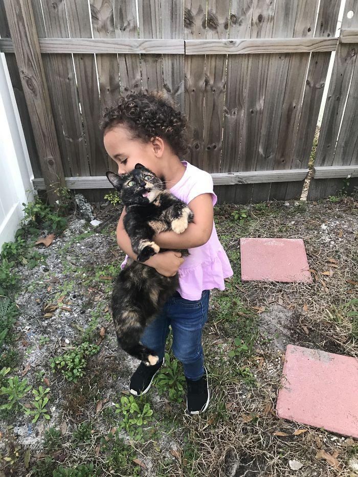 little girl holding freaked-out-looking calico cat