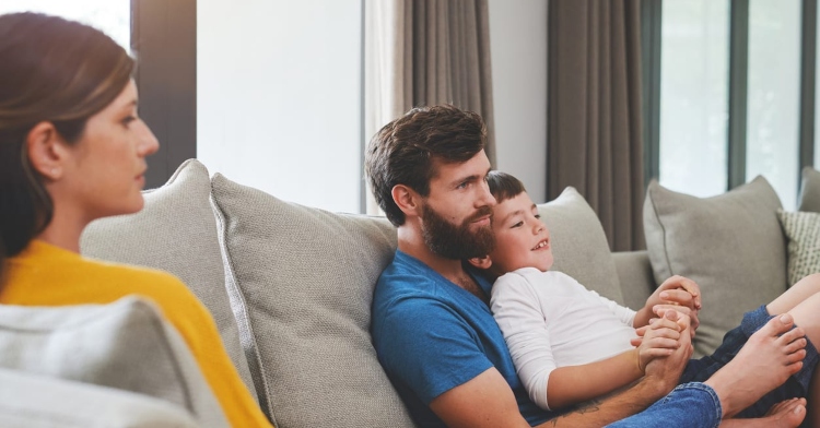 couple sitting separated on the couch with child in dad's lap