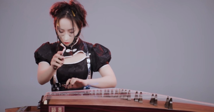 moyun concentrating as she plays the guzheng while wearing a face mask that looks like a fairly realistic face.