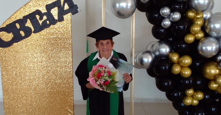 irma esquivel wearing her graduation gown and holding a flower bouquet on one hand and her high school diploma on another.