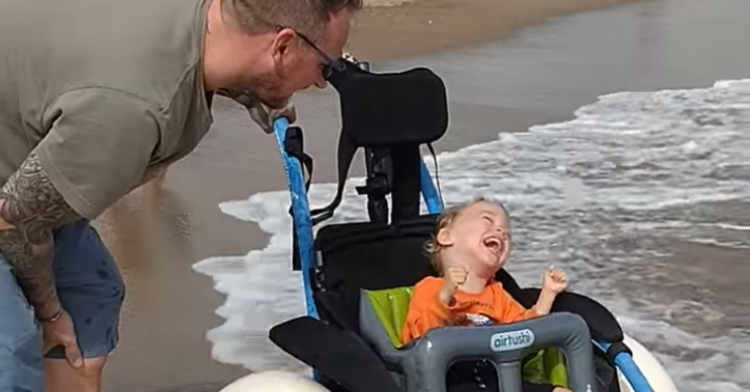 joey enjoying the beach in his wheelchair with his dad on his side