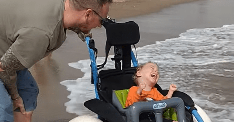 joey enjoying the beach in his wheelchair with his dad on his side