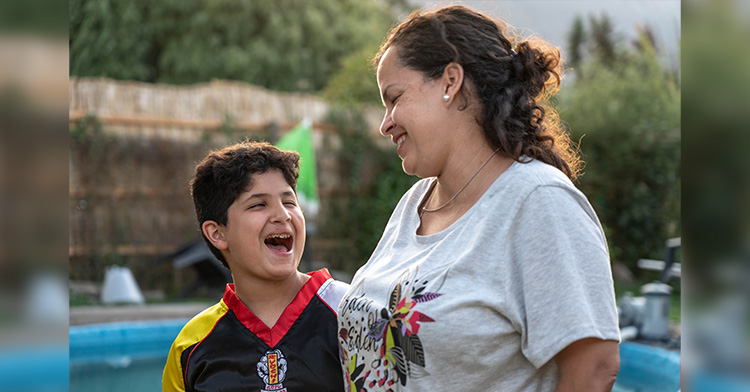 juan laughing with his mouth wide open as his mom stands with him, smiling at him.