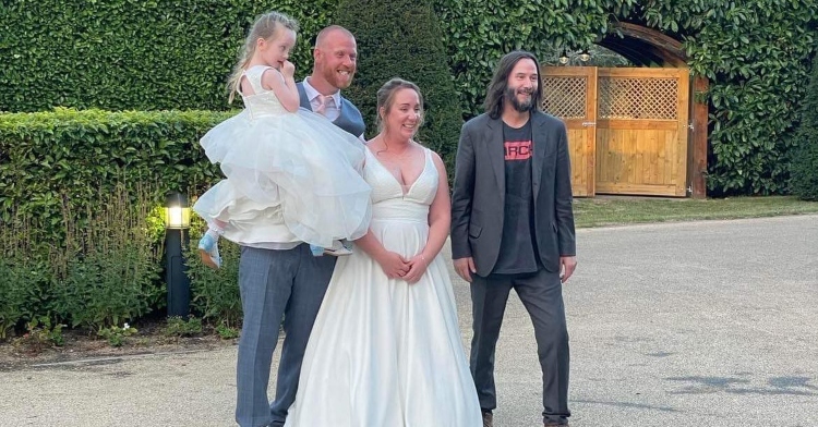 james and nikki roadnight smiling as they pose with actor keanu reeves. james is holding a little girl in his arms, and they’re posing outside.