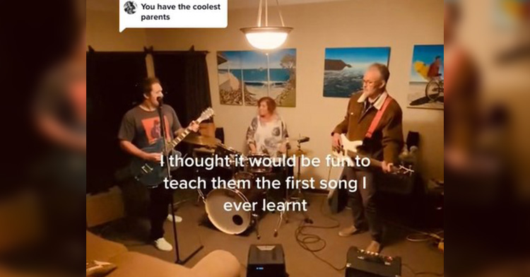 ryan stokes, his dad, and his mom, andrea, playing music together in their home. ryan plays guitar while singing at a microphone. andrea plays the drums. dad plays bass.