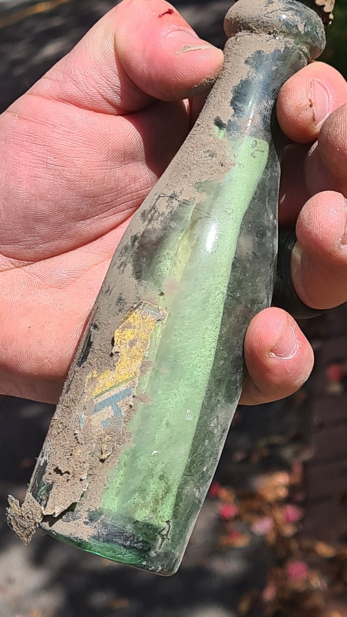 closeup of someone's hand holding an old, dirty green bottle with a letter inside.