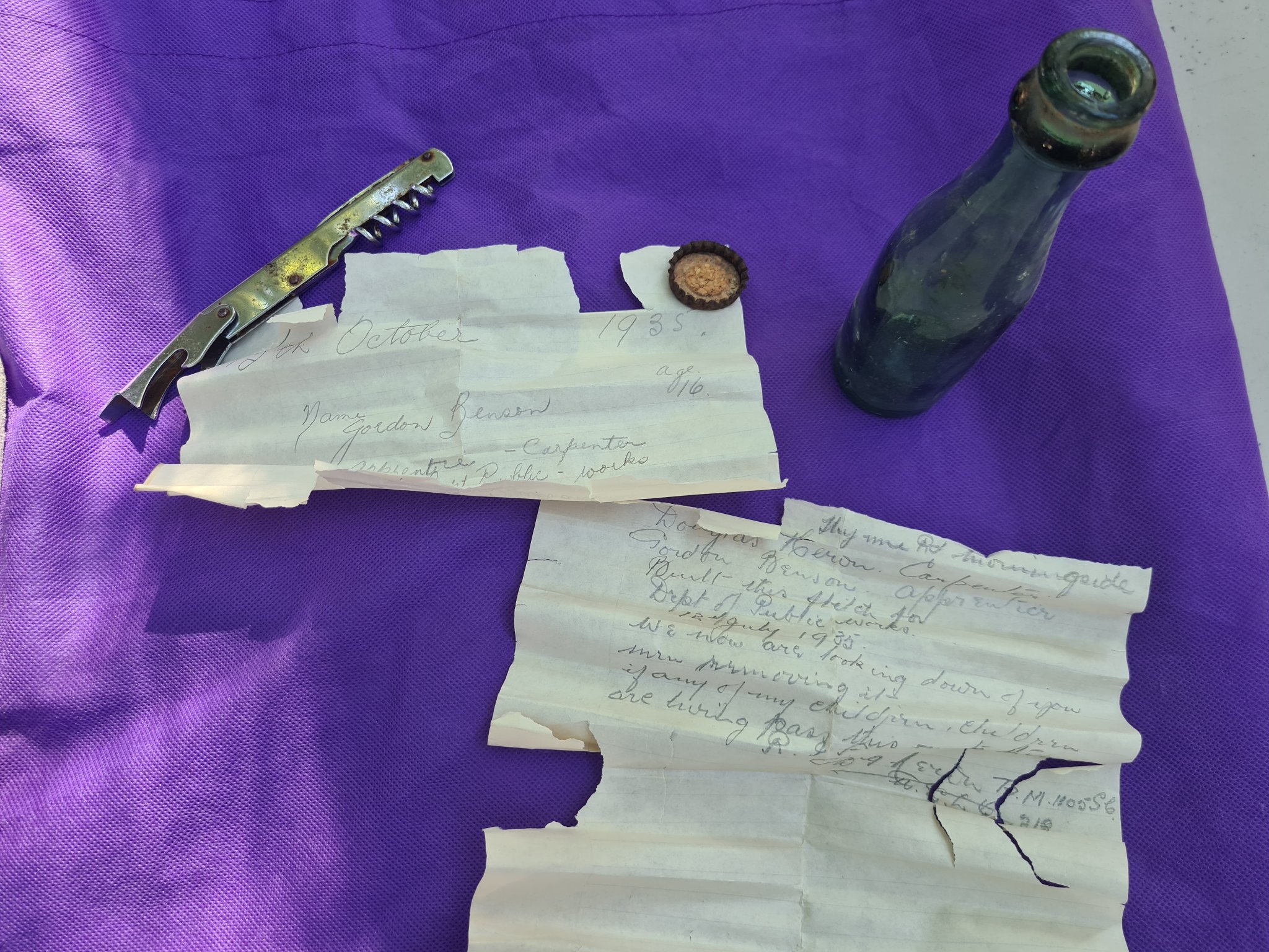 an older letter from 1935, written by gordon benson. the letters are laying on a purple table cloth next to the old, green bottle it was in and the bottle's cap.