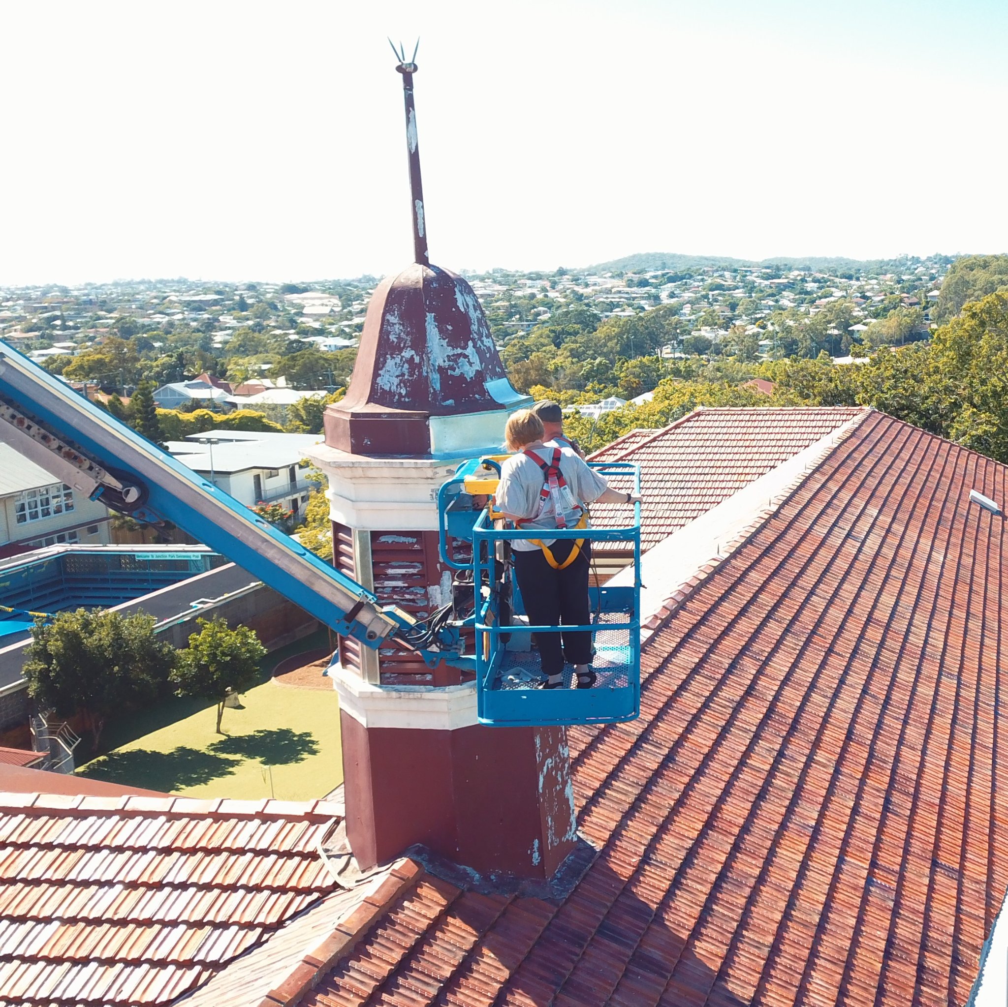 two workers on a lift as they inspect a spire at the junction park state school in australia. 