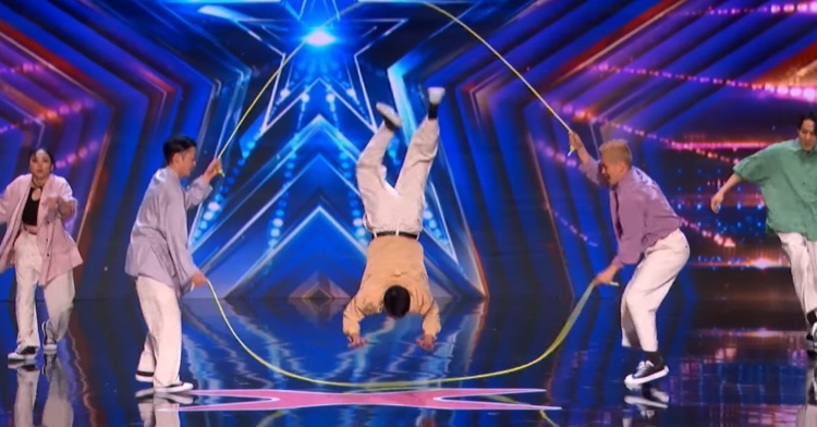 waffle, the double dutch crew from japan, performing on “america’s got talent.” two of them are holding two ropes as one of them is mid-air while getting into a hand-stand position between the ropes. there’s one member on each side of the jump rope holder’s who are dancing.