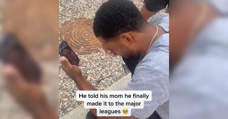 wynton bernard squatting outside as he facetimes his mom. he's wiping his eyes with one hand as he cries tears of joy.