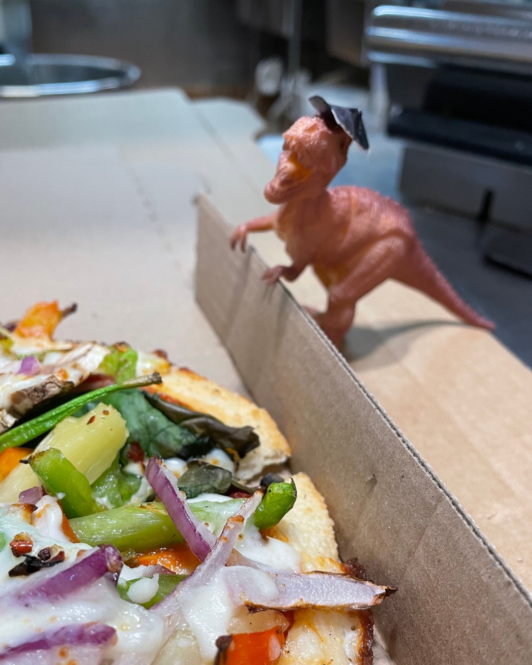 Bitey the dinosaur toy posing with a freshly made Domino's pizza.