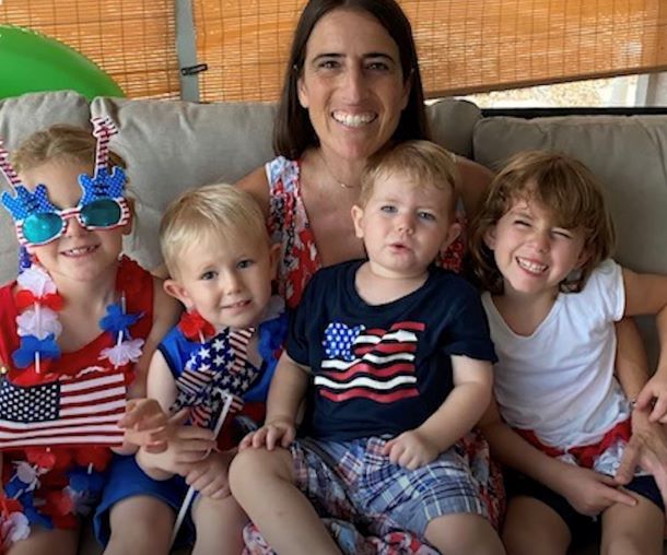 Mother smiling with her four children while sitting on a couch. They are all wearing Fourth of July clothes