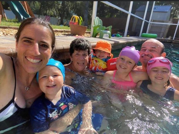 Mother smiling in the pool alongside her children and family.