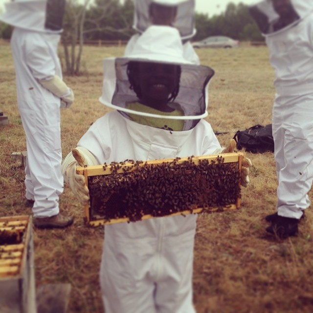 Mikaila Ulmer dressed in beekeeper garb as a kid. She's smiling as she holds a case covered in bees.