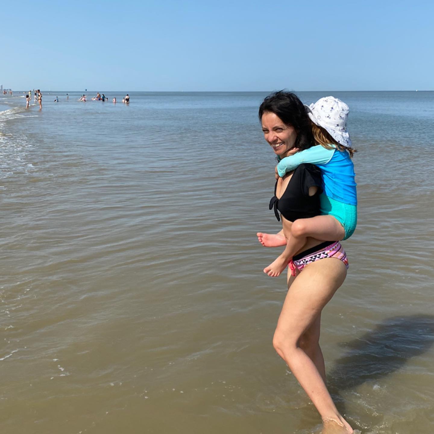 Sarah Talbi carries her daughter Lilia on her back at the beach.