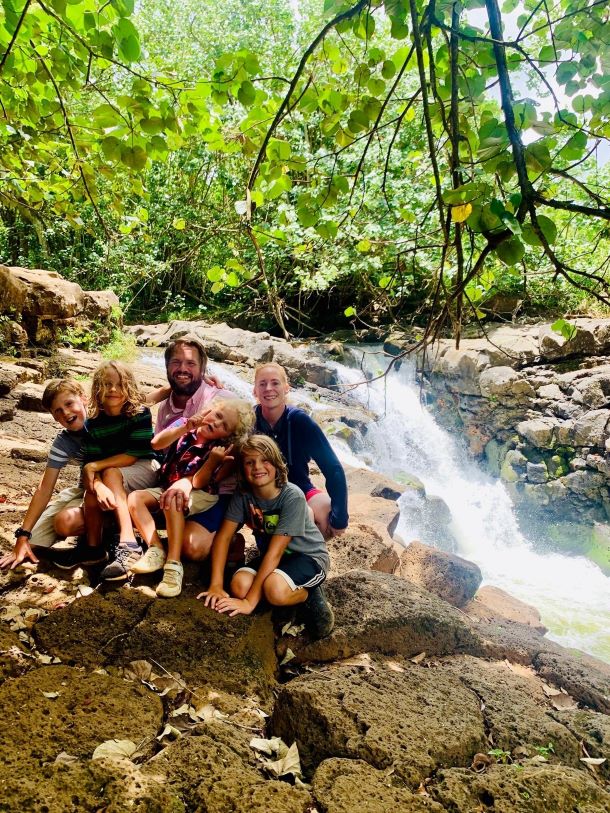 Tiberius family smiles in photo taken out in nature near a waterfall.