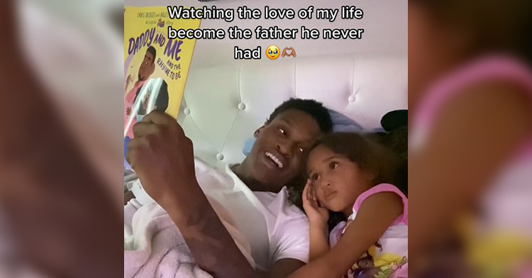 dave bell and his daughter laying in bed as he reads her a book. dave is holding the book up into he air for both of them to see. the name of the book is “daddy and me and the rhyme to be.” dave is looking over at her as he smiles and she’s intensely staring at the book.