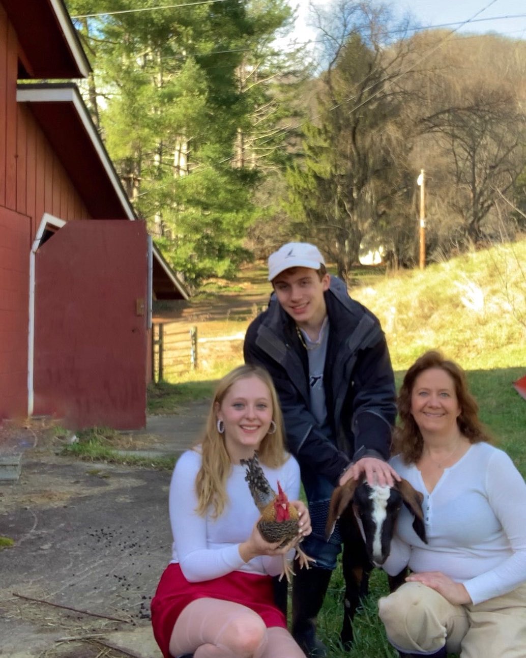 Alexa, a guy named Nick, Sharon, Chester the chicken, and Stella goat posing together for a photo at Friendly Fields Farm. A red building is just in the distance behind them.