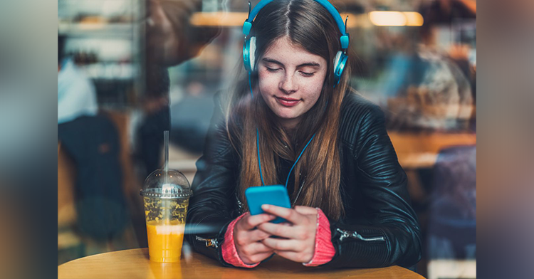 girl wearing headphones and texting on her phone at a table