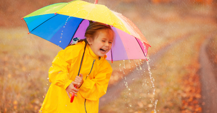 little girl laughing while holding an umbrella while it's raining.