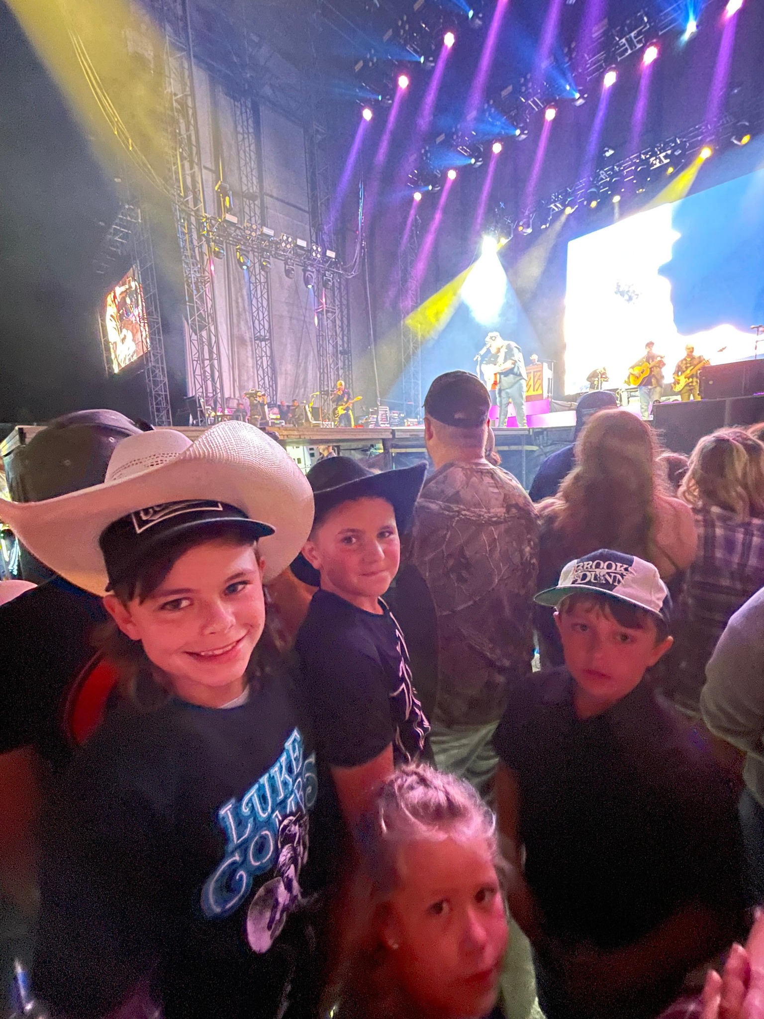 bo fenderson, tanner, and two other kids posing for a photo at the luke combs concert. the stage is just a few feet away from them.