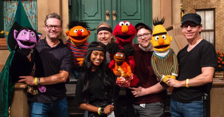 megan holding her muppet gabrielle and other cast members of sesame street holding their muppets.