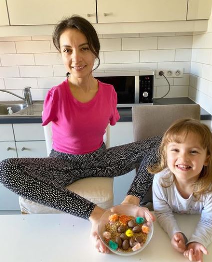 Sarah talbi sits next to the counter holding a bowl with her feet, her daughter sits next to her